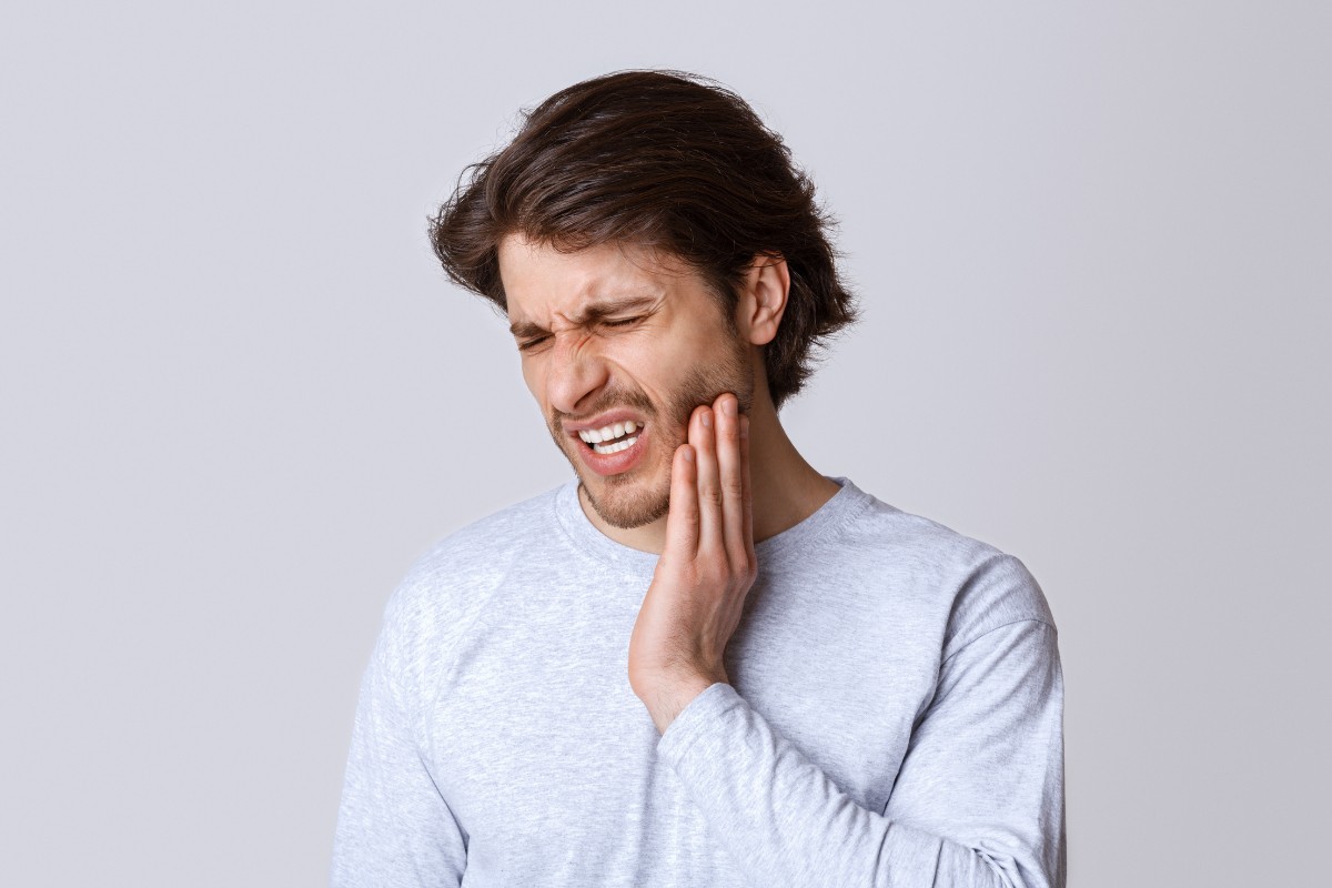 Man holding cheek in pain against white background, depicting dental discomfort or toothache.