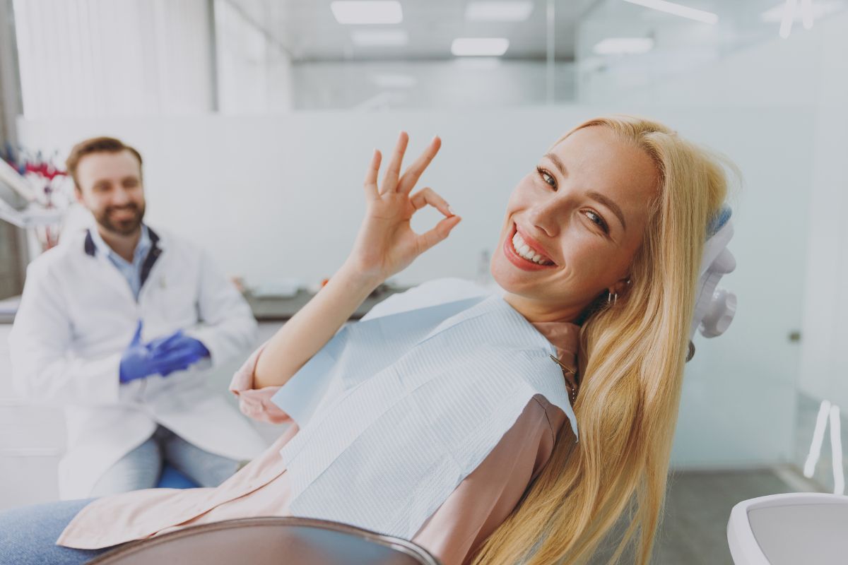 How Often Should You Visit the Dentist Happy female patient in dental chair giving thumbs up with dentist in background at clinic.